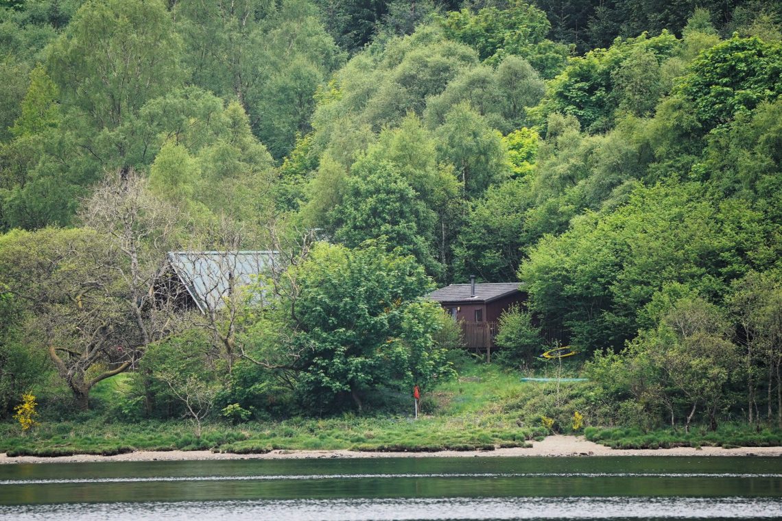 A secluded cabin beside a peaceful Scottish lake surrounded by woodland