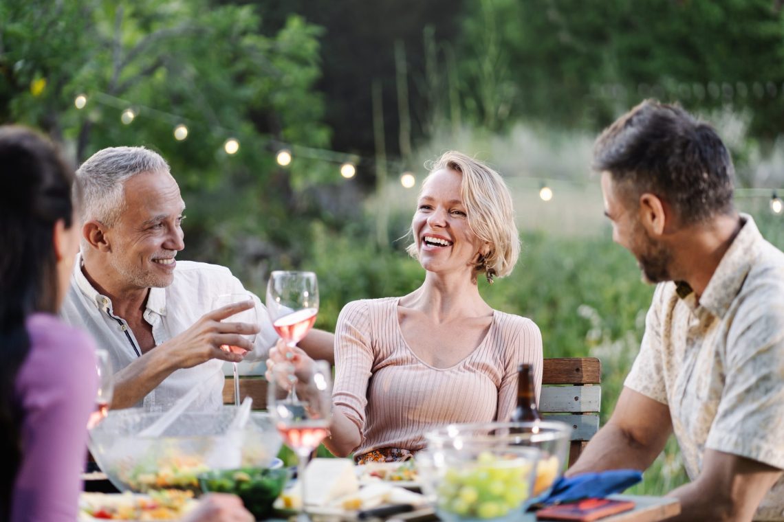 Mature friends sharing dinner and wine around a garden table