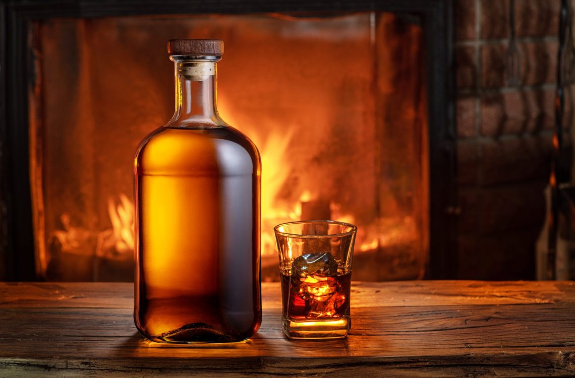 Whisky glass and bottle on a wooden table beside a fire