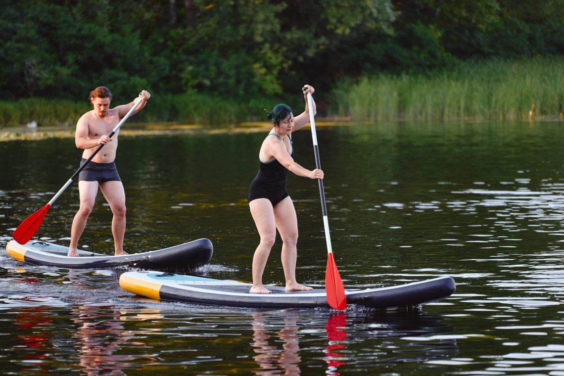 Couple paddleboarding on a calm lake surrounded by forest